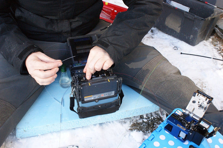 Field technician splicing fiber with a fusion splicer, cleaver, and tool kit