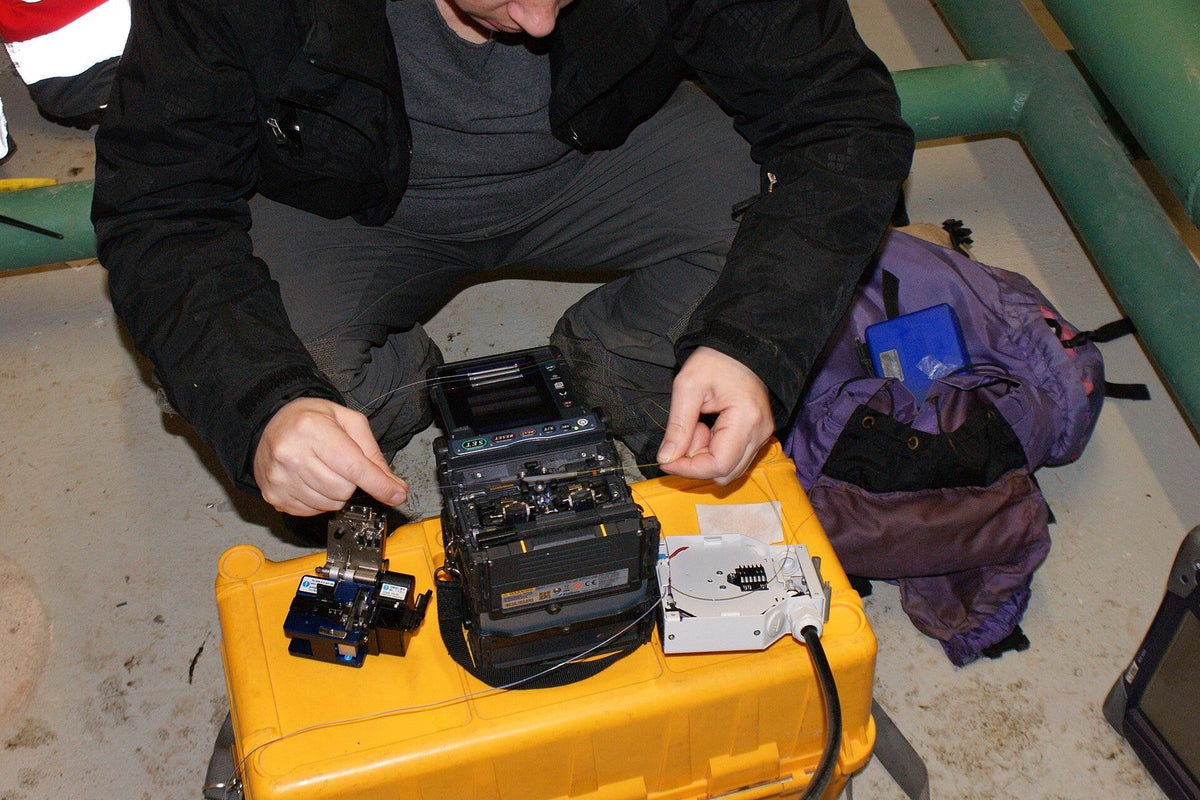 Technician testing and splicing fiber in a plant room with a handheld optical tester