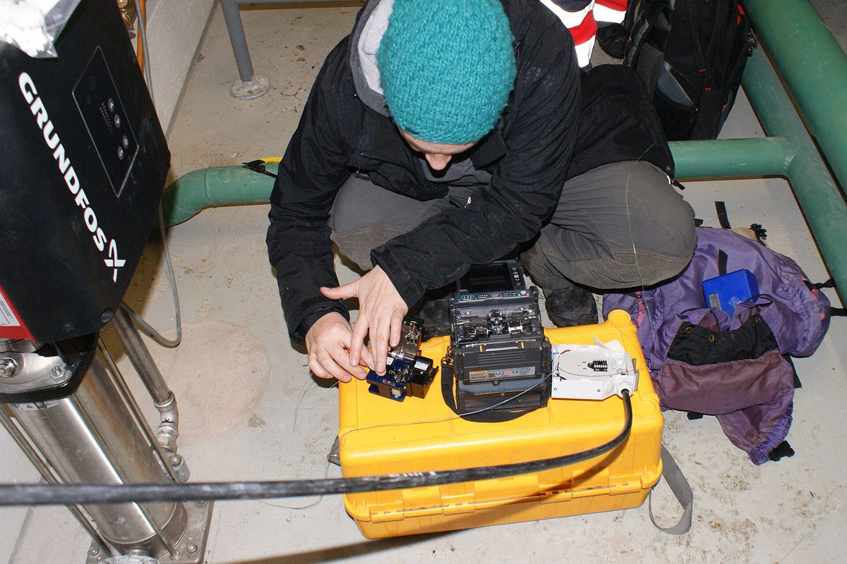 FTTH technician preparing fiber with a splicer, cleaver, and tool case